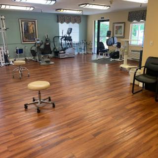 A spacious therapy room equipped with fitness machines and a polished wooden floor.
