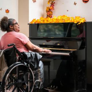 A person in a wheelchair playing the piano, surrounded by autumn decorations.