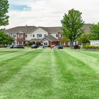 A well-maintained lawn leading up to a residential building with trees and a clear sky.