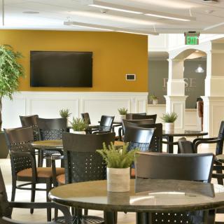 A modern dining area with tables and chairs, featuring a television and decorative plants.
