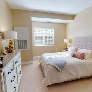 A cozy bedroom with neutral tones, featuring a bed, nightstands, and a large window allowing natural light.