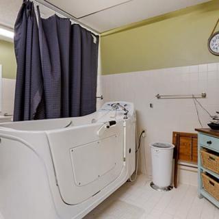 A bathroom featuring a walk-in bathtub with a dark curtain, sink, and wall-mounted clock.