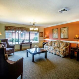A cozy living room with a sofa, armchairs, and a coffee table, complemented by warm lighting and decorative art on the walls.