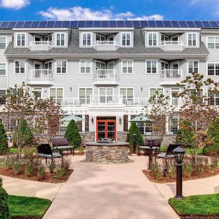 A modern apartment building with solar panels, featuring a landscaped garden and outdoor patio area.