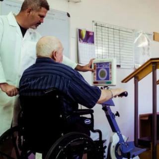 A healthcare professional assists a patient in a wheelchair using a rehabilitation device.