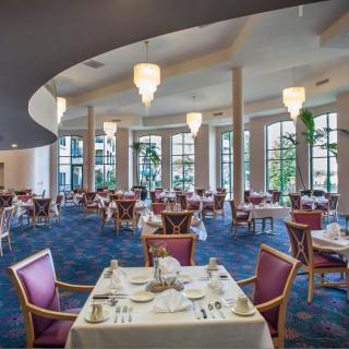 An elegant dining room with beautifully set tables and ample natural lighting through large windows.
