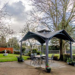 A gazebo set in a garden with patio furniture under cloudy skies.