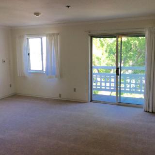 A bright living room with a window and sliding doors leading to a balcony.