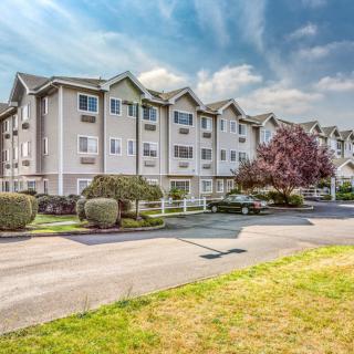 A exterior view of a multi-story apartment building with landscaped surroundings and a parking area on a sunny day.