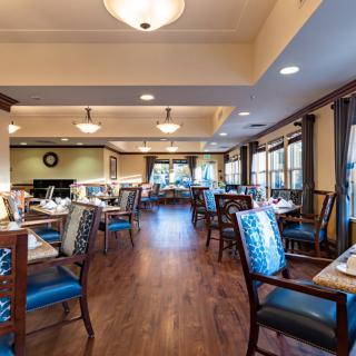 A spacious and elegantly designed restaurant dining room with neatly arranged tables and chairs, featuring warm lighting and wood flooring.