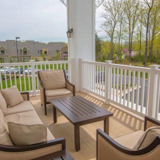 A cozy patio with cushioned chairs and a table, overlooking a parking area and greenery.