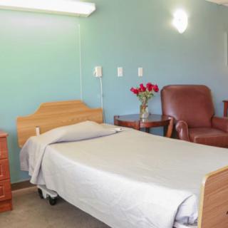 A hospital room with a bed, chair, and vase of roses.