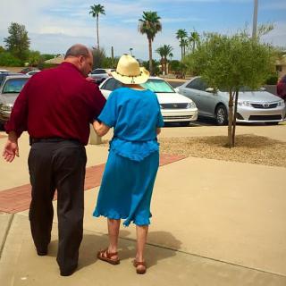 An elderly couple walking together in a parking lot on a sunny day.