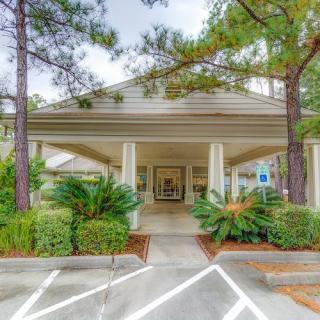Entrance of a building with surrounding trees and parking spaces.