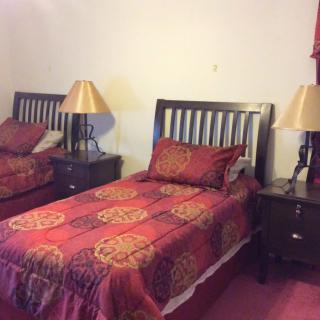 A cozy bedroom with twin beds, adorned with patterned red bedding and flanked by nightstands and lamps.