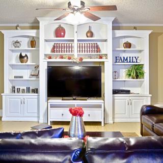 A cozy living room with a large entertainment center featuring a television, bookshelves, and decorative items.