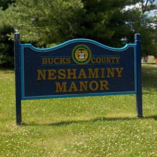 A sign for Neshaminy Manor in Bucks County, set against a backdrop of grass and trees.