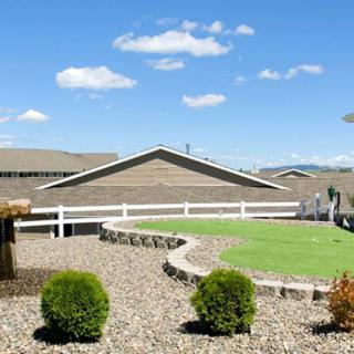 A landscaped garden with shrubs, a stone pathway, and a white fence under a clear blue sky.