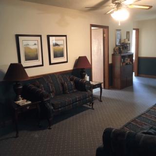 A cozy living room with a dark sofa, matching lamps, framed wall art, and a ceiling fan.