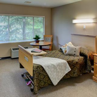 A well-lit hospital room with a single bed, chair, and table by the window.
