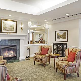 A cozy living room with armchairs and a fireplace, adorned with artwork on the walls.