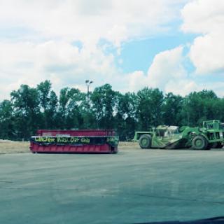 A vibrant pink and green heavy machinery parked outdoors, surrounded by trees and under a cloudy sky.
