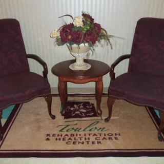 A cozy seating area with two burgundy chairs, a wooden table, and a floral arrangement on display.