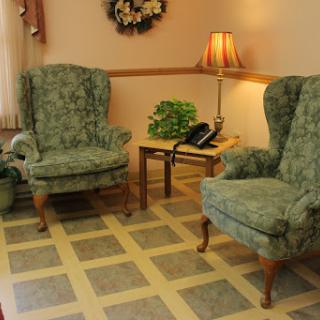 A cozy living room setup featuring two green upholstered armchairs and a small table with a lamp and a telephone.