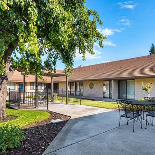 A peaceful courtyard with a pathway, patio furniture, and lush greenery surrounding a building.