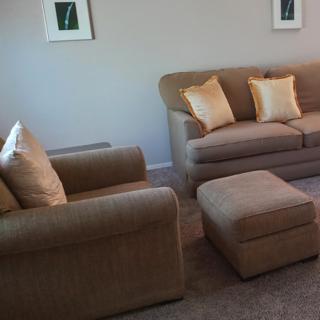A cozy living room with a sofa, armchair, and ottoman adorned with cushions.