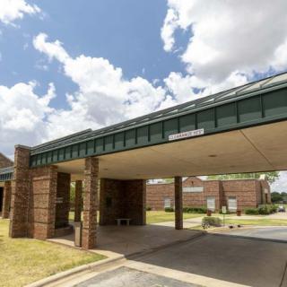A building entrance with a covered driveway under a partly cloudy sky.