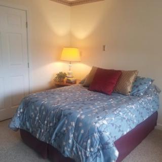 A cozy bedroom with a neatly made bed, accented by decorative pillows and illuminated by a warm lamp.
