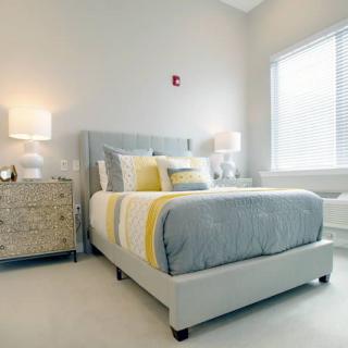 A modern and minimalist bedroom featuring a neatly made bed with gray and yellow bedding, flanked by two lamps on a wooden nightstand.