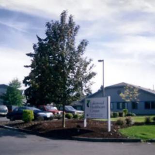 A building with a surrounding parking lot and a sign in front, accompanied by trees under a clear sky.
