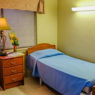 A simple and functional hospital room featuring a single bed, nightstand, and a lamp.