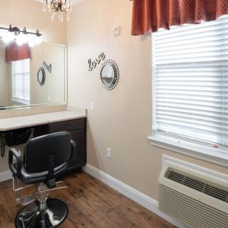 An empty hair salon room with a styling chair, mirror, and window.