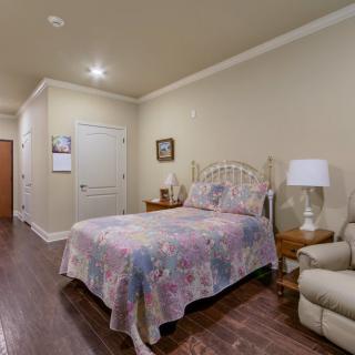 A cozy bedroom with a floral bedspread, wooden floors, and comfortable seating.