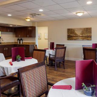 A cozy restaurant dining area with neatly arranged tables and chairs, featuring a glimpse of the kitchen in the background.