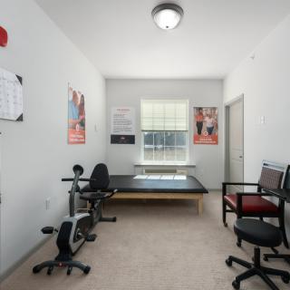 A well-lit physical therapy room with exercise equipment, posters, and seating.