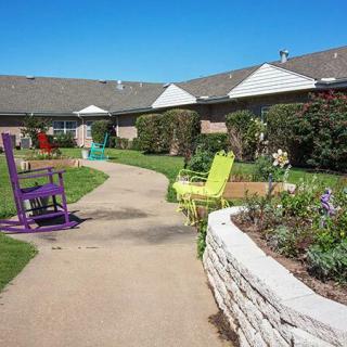 A serene garden pathway with colorful chairs and lush greenery.