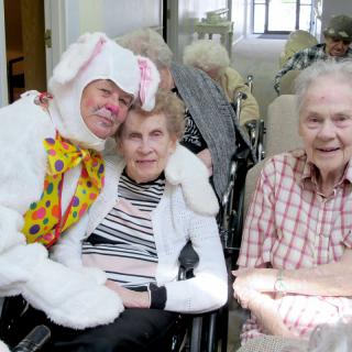 A person in a bunny costume poses with elderly residents in a nursing home, sharing a joyful moment.
