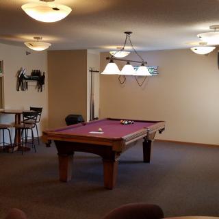 A cozy recreational room featuring a pool table with overhead lighting and seating areas.
