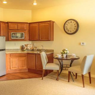 A cozy kitchen and dining area featuring wooden cabinets, a small round table with two chairs, a refrigerator, and a microwave.