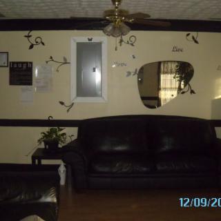 A cozy living room with a black leather sofa, decorative wall art, and a ceiling fan.
