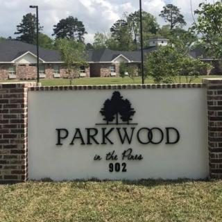 Entrance sign for Parkwood community with brick wall and trees in the background.