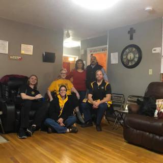 A group of people gathered in a living room, sitting and standing in a casual setting.