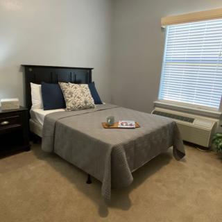 A cozy bedroom with a neatly made bed, nightstand, and window.