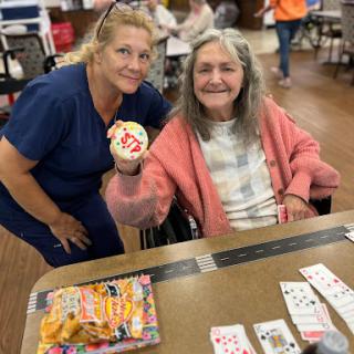 A caregiver shares a joyful moment with an elderly woman, celebrating with a decorated cookie during a fun activity.
