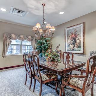 A traditionally decorated dining room with a chandelier hanging over a polished wood table and chairs, featuring artwork on the wall.
