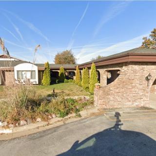 A suburban brick house with a driveway and small garden under a clear blue sky.